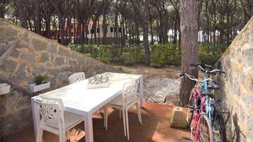 An outdoor patio with a stone wall, a white table, and chairs. A bicycle is parked against the wall.
