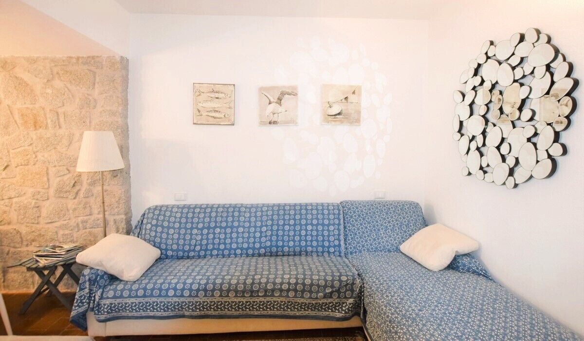 A room with a blue patterned sofa, a stone wall, and three framed artworks on the wall.
