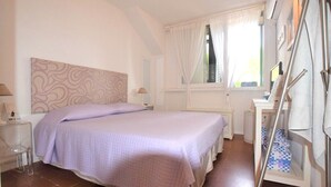 A bedroom with a bed, bedside tables, a window with curtains, and a mirror.