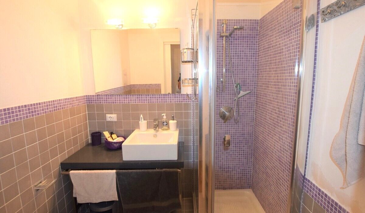 Une salle de bain avec une douche à parois de verre, un lavabo avec un miroir et des murs carrelés.