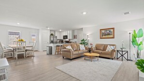 A modern living room with a beige sofa, a coffee table, and a dining area with a white table and chairs.