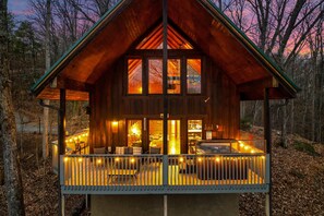 A wooden cabin with a balcony, large windows, and a porch area.