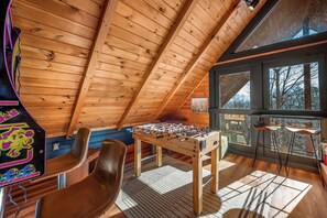 A cozy room with a wooden ceiling, a foosball table, and a window with a view.