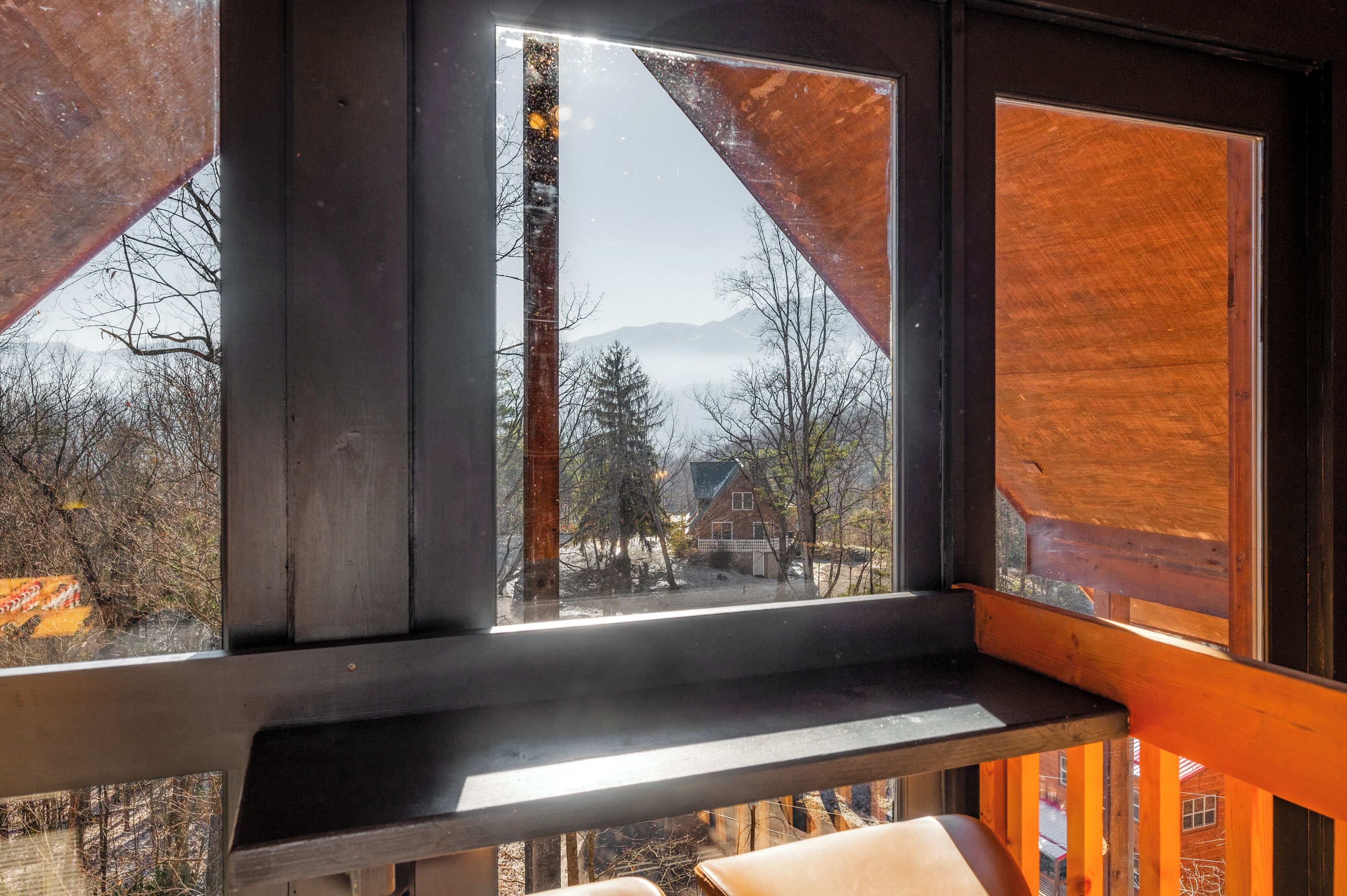 A room with a large window overlooking a snowy landscape, a wooden bench, and a view of a house and trees.