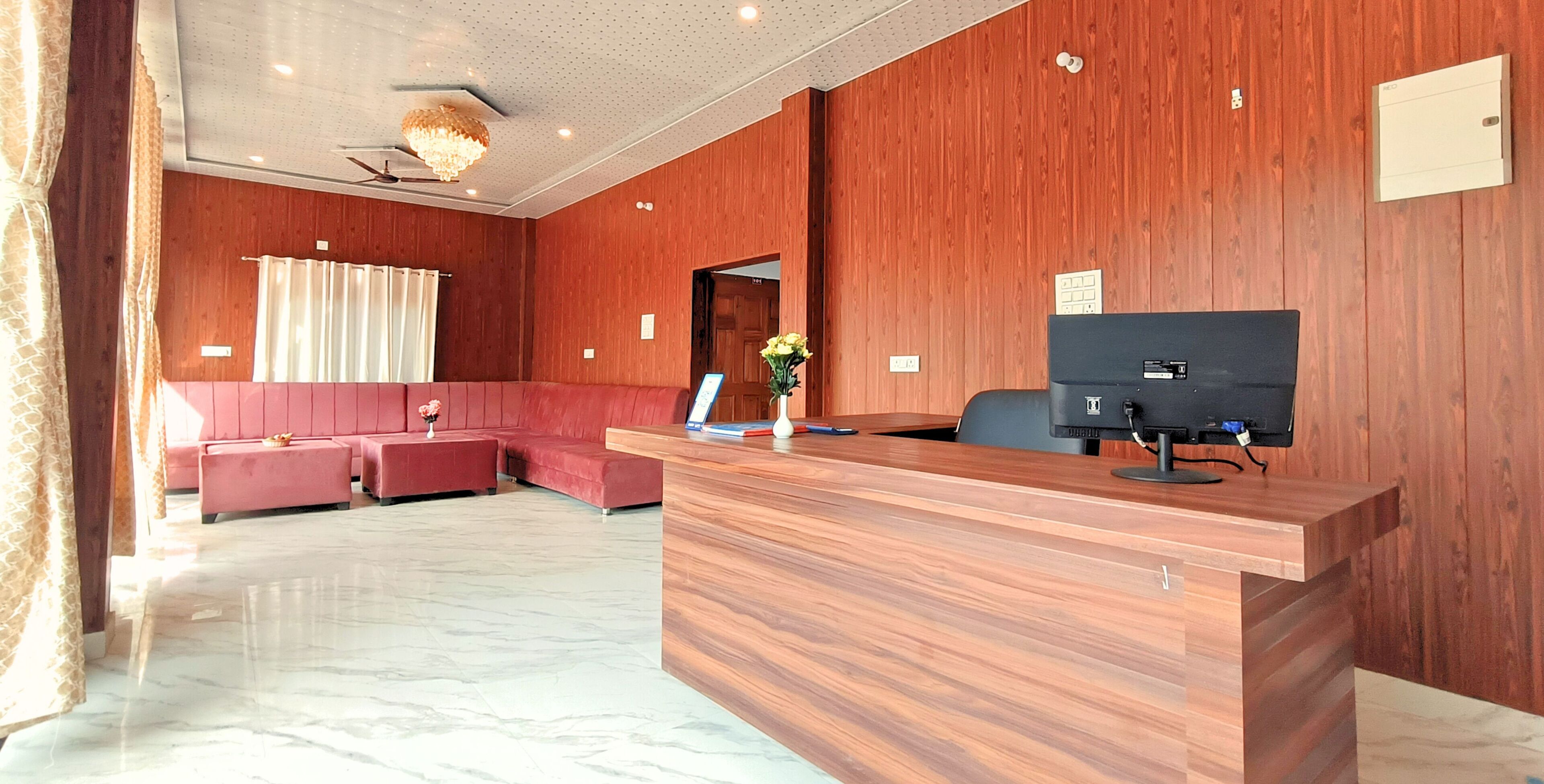 A hotel lobby with a reception desk, a red sofa set, a chandelier, and a wooden wall.