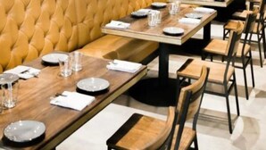 A restaurant with wooden tables and chairs, a tufted yellow sofa, and a clean, modern design. - Maa Mandakini Resort By Asapian Hotels (Karwi)