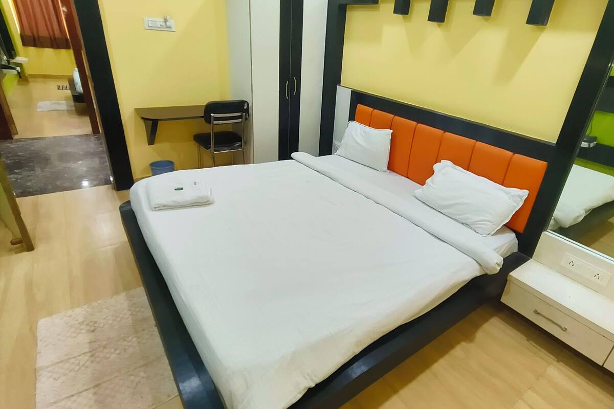 A neatly made bed with white bedding and an orange headboard in a hotel room.