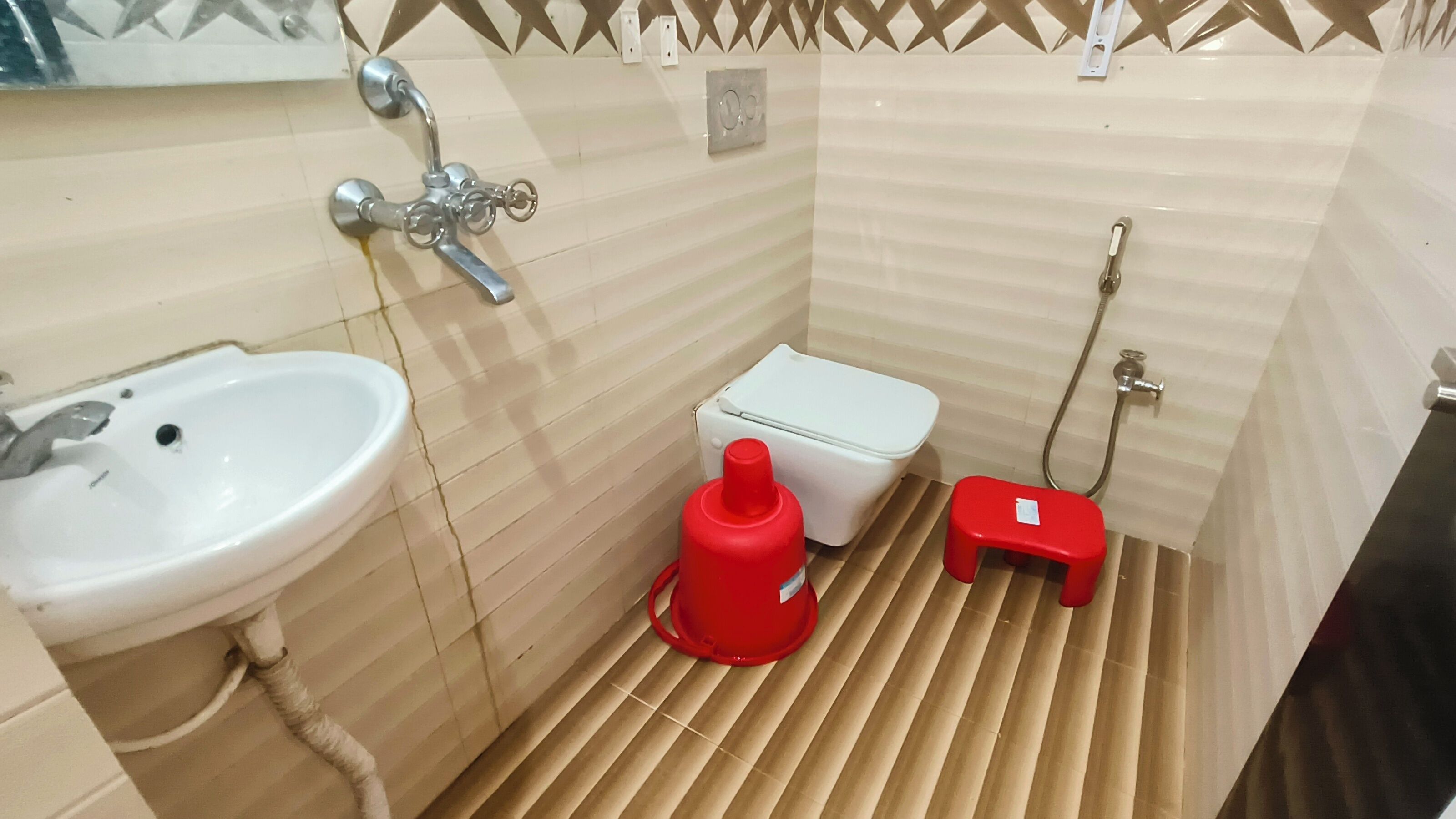 A small bathroom with a white sink, a toilet, and a red bucket.