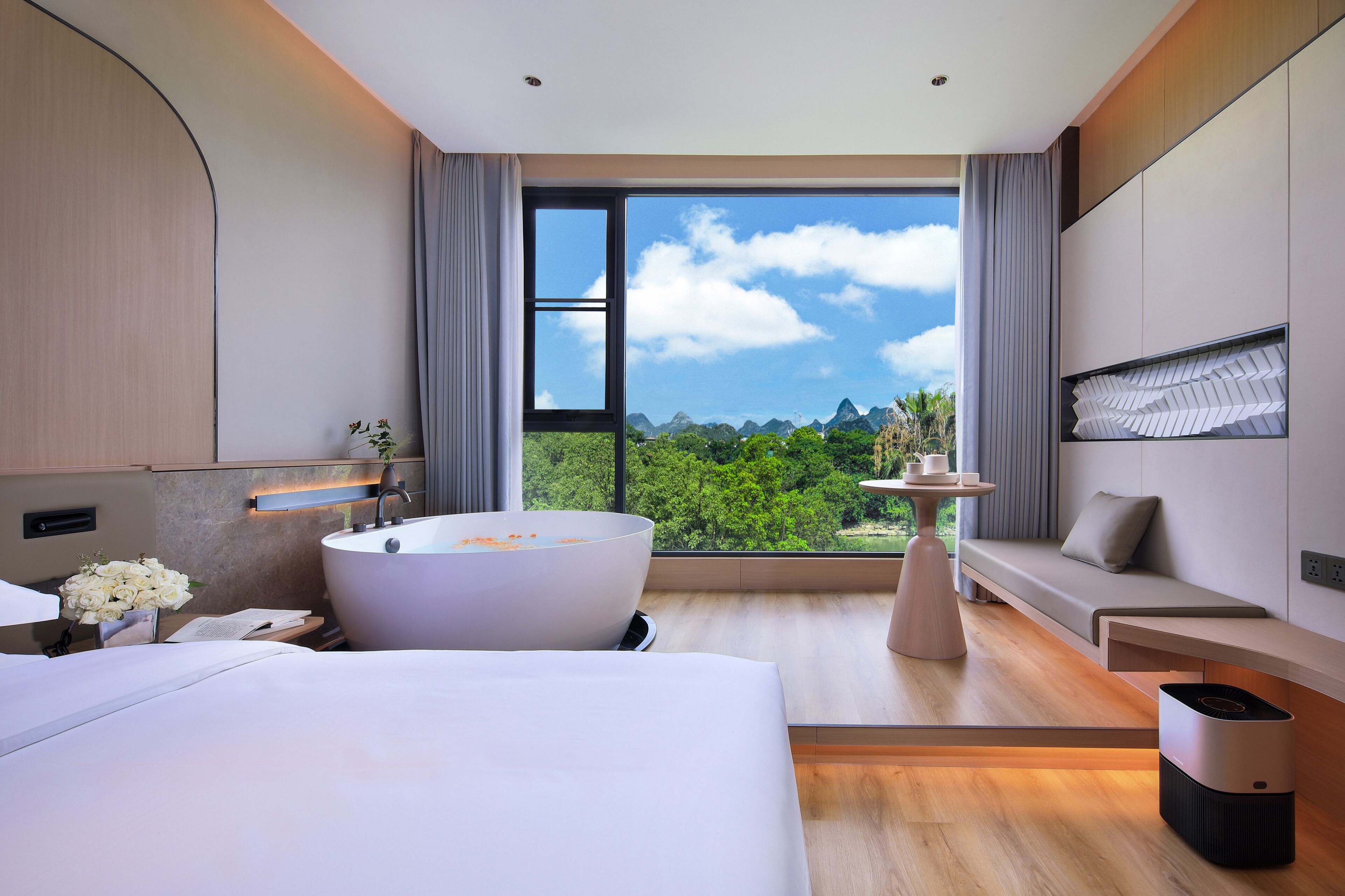 Habitación de hotel moderna con una bañera grande, un sofá, una mesa de comedor y vistas a vegetación exuberante.
