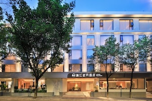 Un hotel moderno con una fachada bien iluminada, amplias ventanas y una entrada visible con escalones que conducen a la puerta.