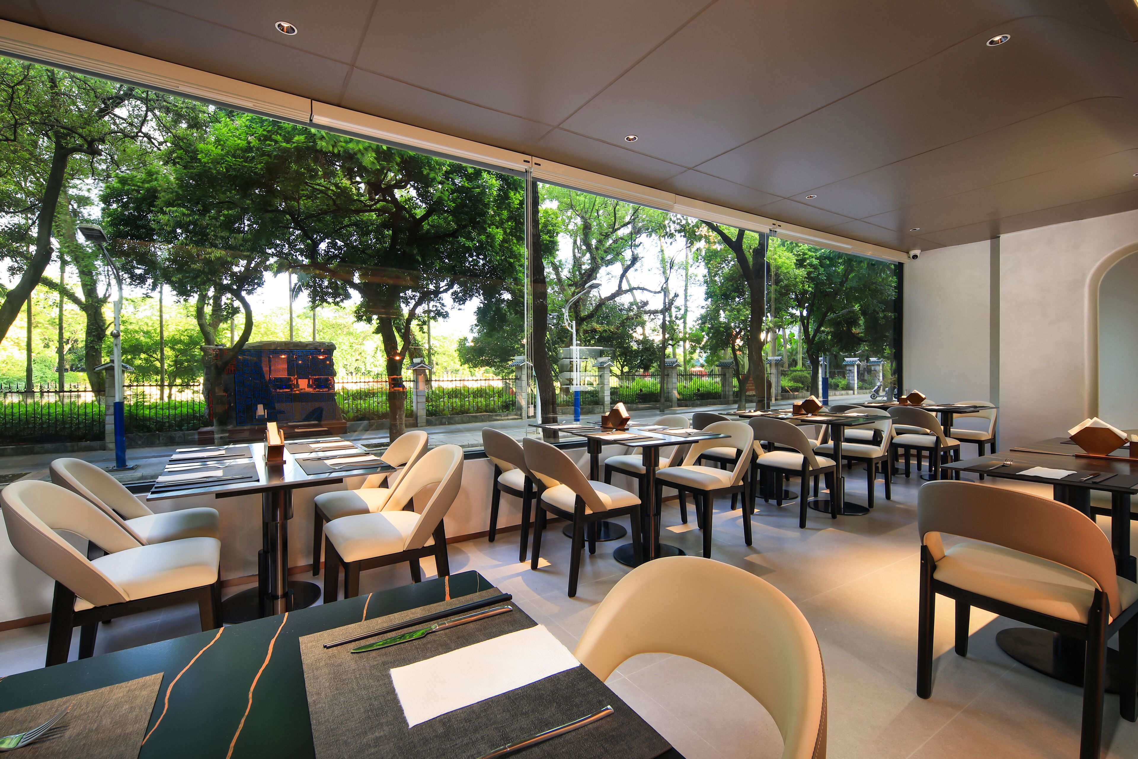 A modern restaurant with indoor seating, large windows, and a view of the outdoors.