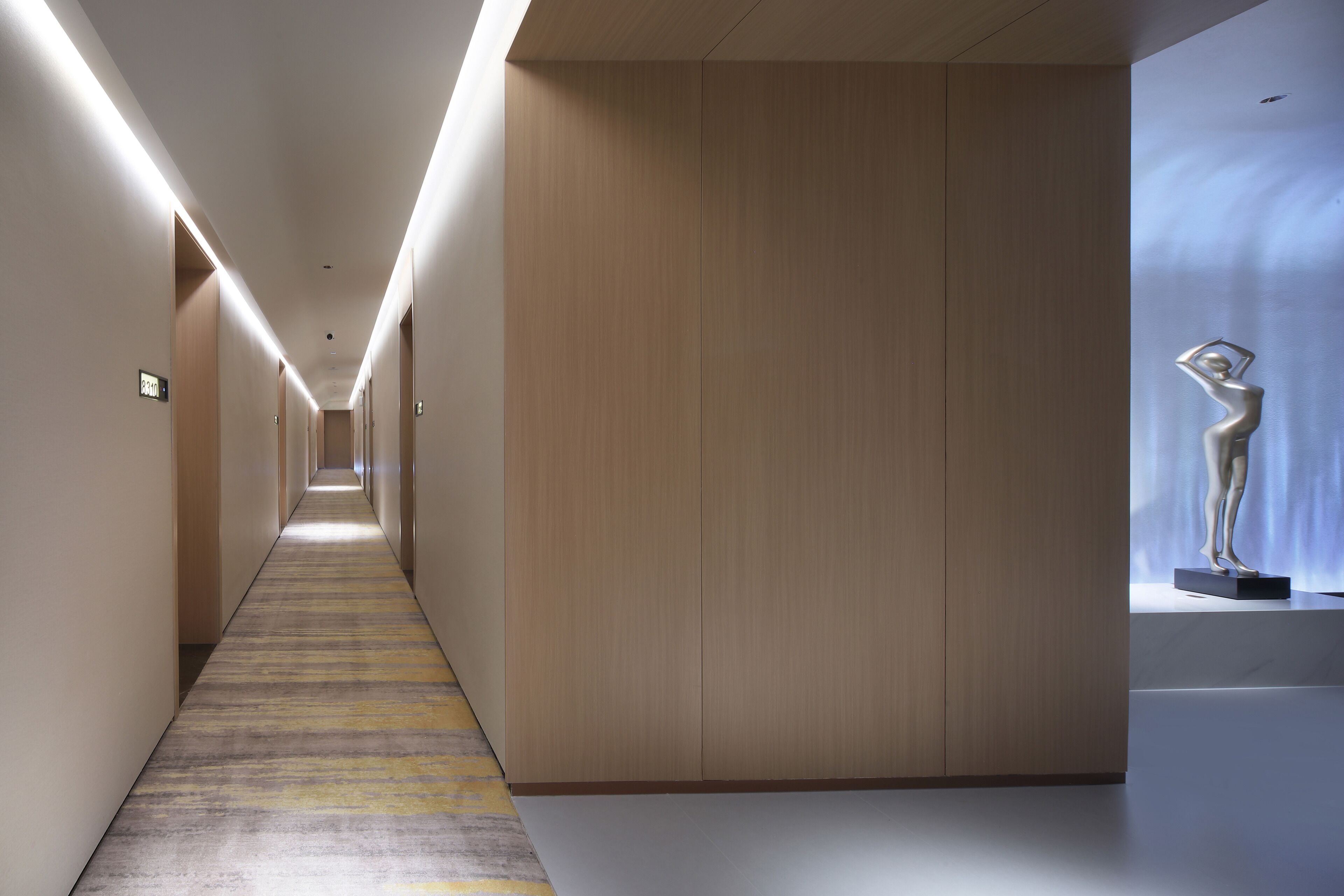 En modern hotellkorridor med en lång, smal hall, träpanel på väggarna och en skulptur som visas upp.