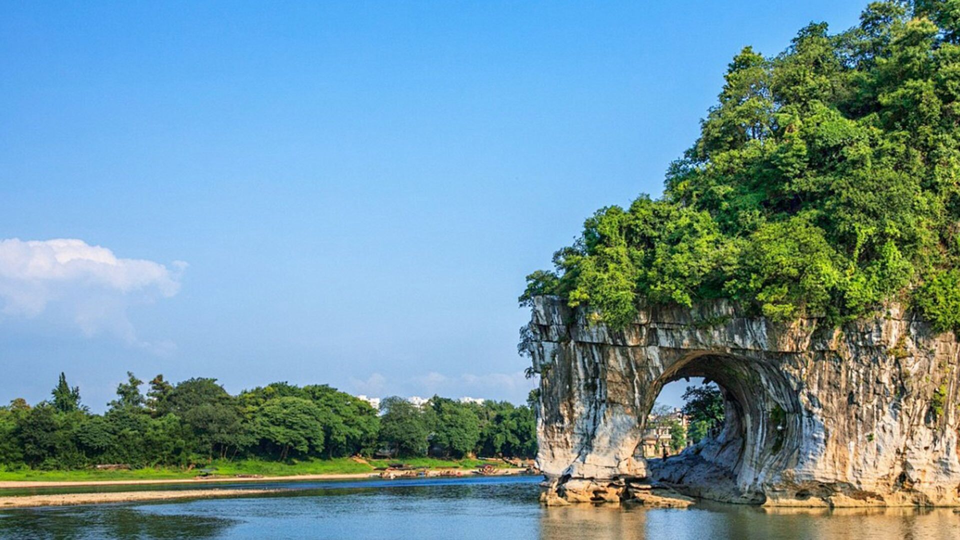 A natural rock arch formation over a river, surrounded by lush greenery and trees.