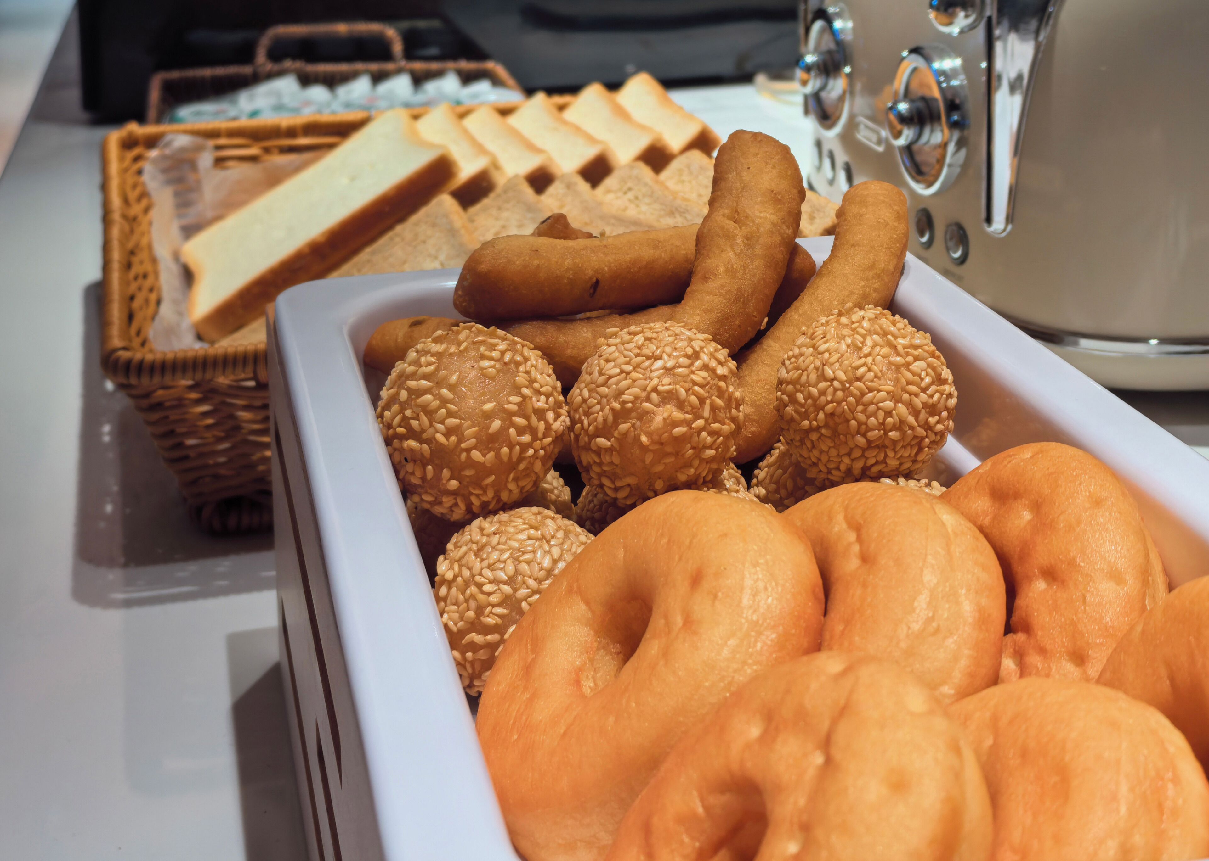 A tray of assorted bread rolls and buns, including sesame seed and plain varieties, displayed on a kitchen counter.