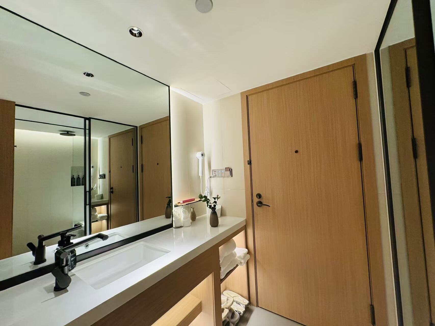A modern bathroom with a large mirror, a white sink, and a wooden door.