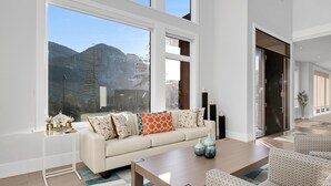 A modern living room with a large window, a sofa, a coffee table, and patterned chairs.