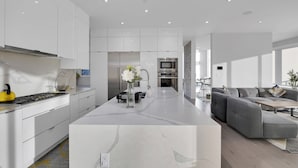 A modern kitchen with white cabinetry, a central island, and a grey sectional sofa in a bright living area.
