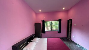 Ein Schlafzimmer mit rosafarbenen Wänden, einem Bett mit weißer und rosa Bettwäsche, einem Kleiderschrank und einem Fenster mit einem Metallgitter.