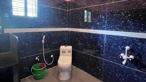 Ein Badezimmer mit Toilette, Dusche und einem grünen Eimer auf dem Boden.