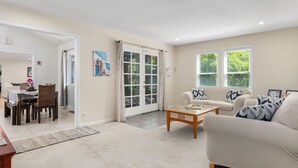 Een ruime woonkamer met een beige bank, een houten salontafel en een eethoek met een tafel en stoelen.