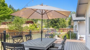 Een terras met een tafel en stoelen, omringd door een houten hek, en een grote parasol die schaduw biedt.