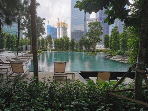 Une piscine entourée de chaises longues, avec une végétation luxuriante et des bâtiments modernes en arrière-plan.
