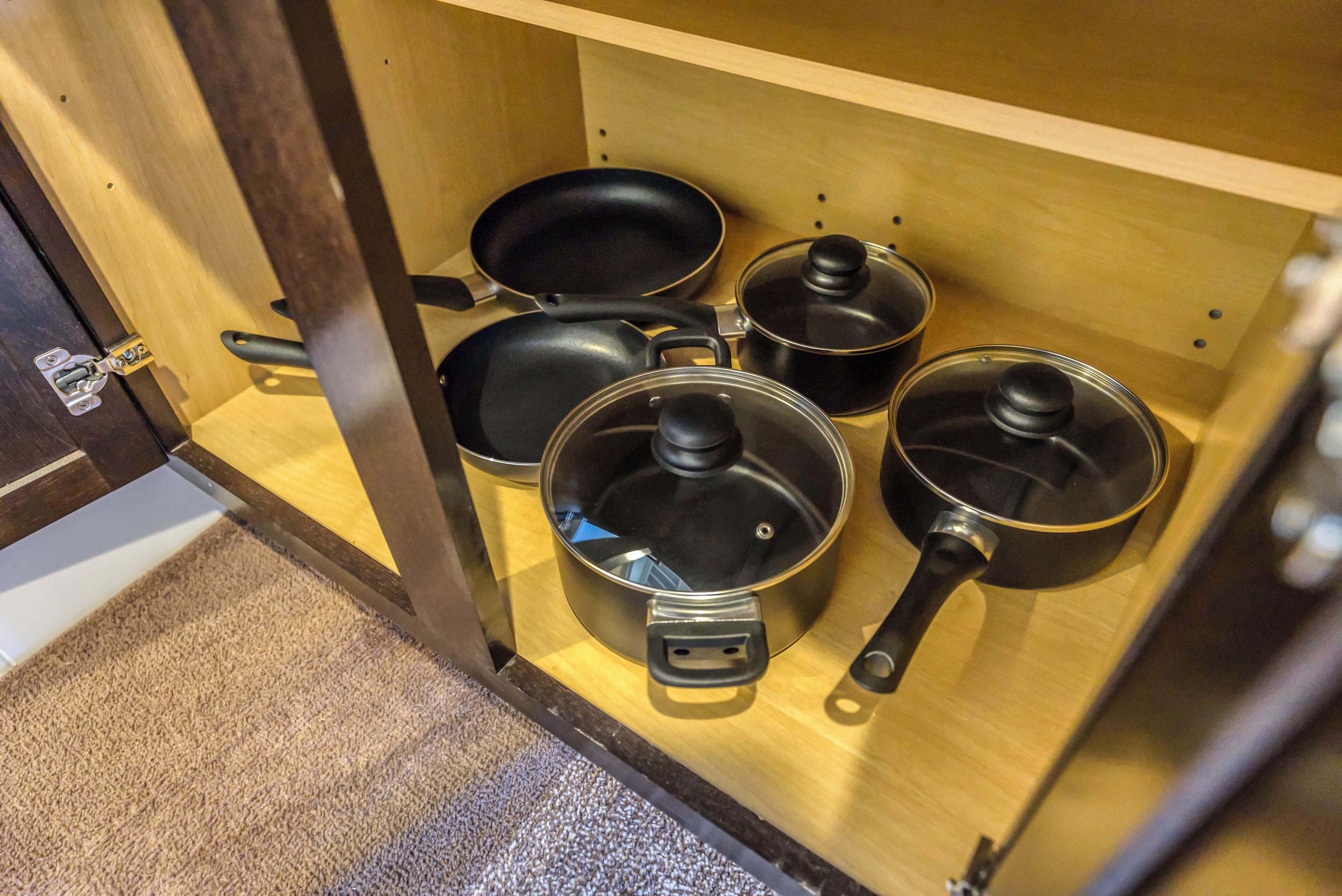 Un armario de cocina con diferentes utensilios de cocina, incluyendo ollas, sartenes y una sartén.
