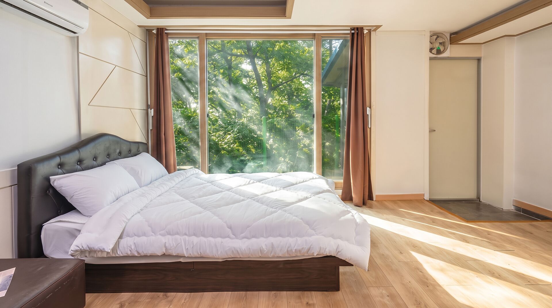 A bedroom with a bed, a window with curtains, and a door.