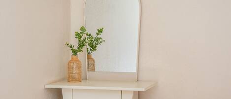 Une coiffeuse blanche, ornée de deux vases en osier contenant des plantes vertes, est placée devant un miroir à cadre blanc.