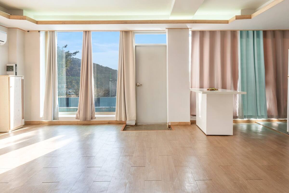 Une pièce spacieuse dotée d’un plancher en bois, d’un bureau blanc et offrant une vue sur une montagne grâce à de grandes fenêtres.