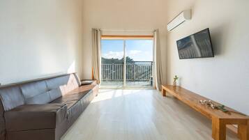 Uma sala de estar moderna com um sofá de couro, um banco de madeira e uma grande janela com vista para uma varanda e árvores.