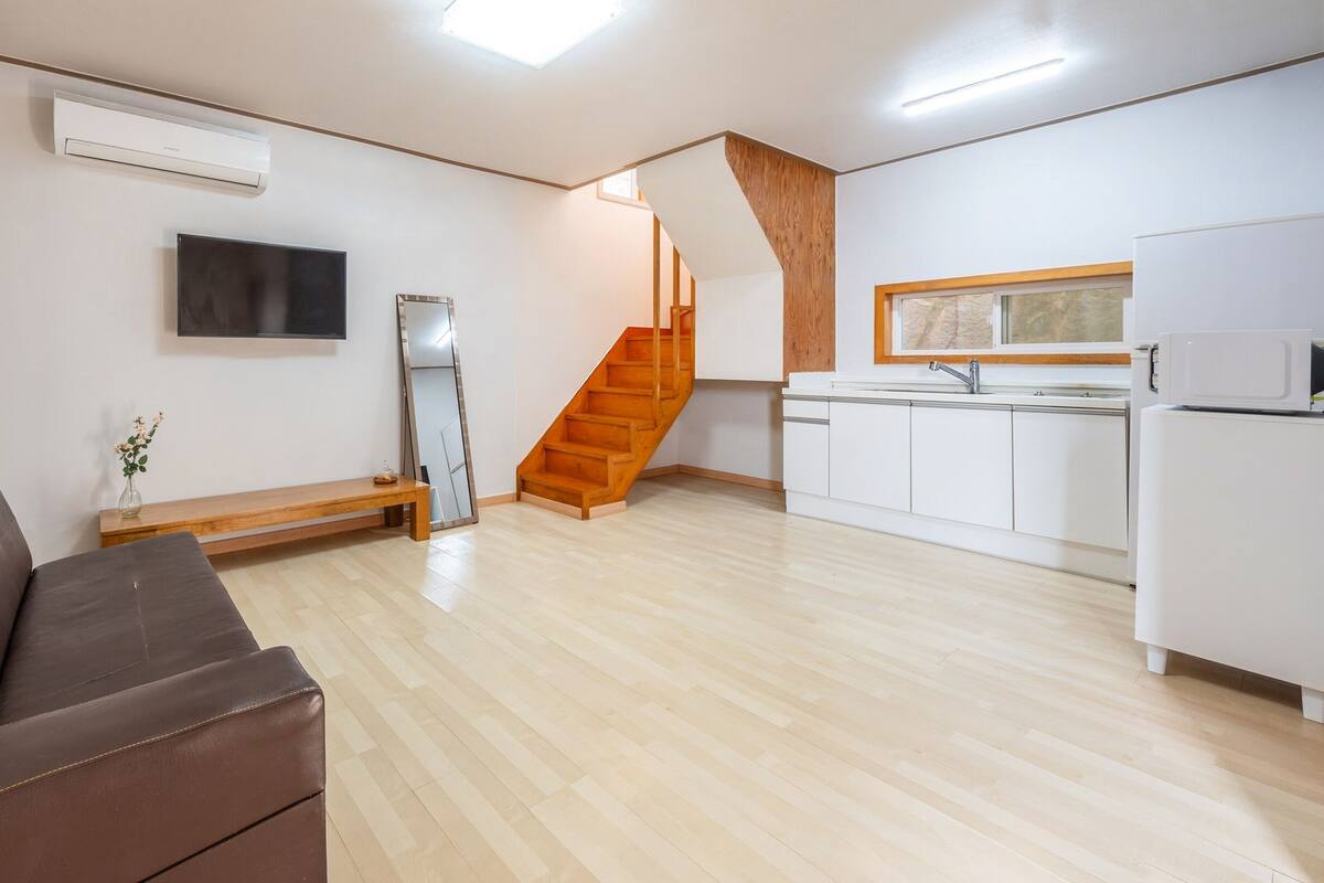 Un appartement moderne doté d’un escalier en bois, d’une cuisine avec des meubles blancs, d’un téléviseur à écran plat et d’un canapé en cuir marron.