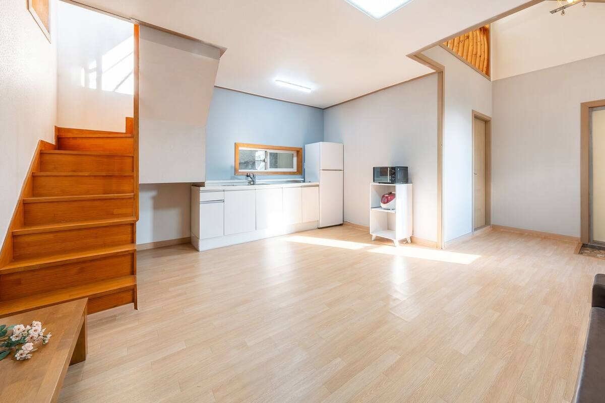Un appartement moderne doté d’un escalier en bois, d’une cuisine avec des meubles blancs, un four à micro-ondes et un réfrigérateur.