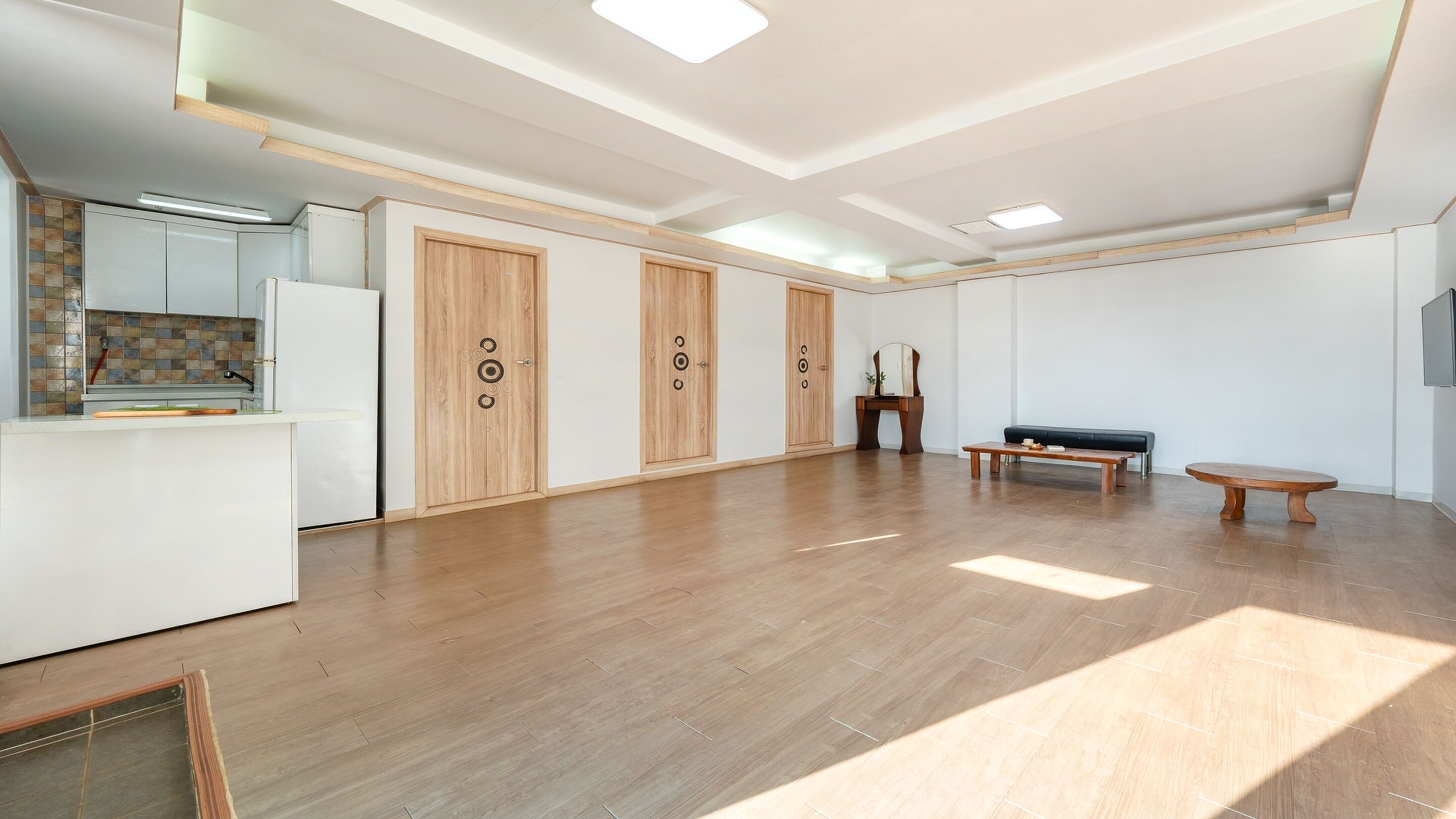 Una habitación amplia con suelo de madera, una zona de cocina y un espacio de estar con un banco y una mesa.