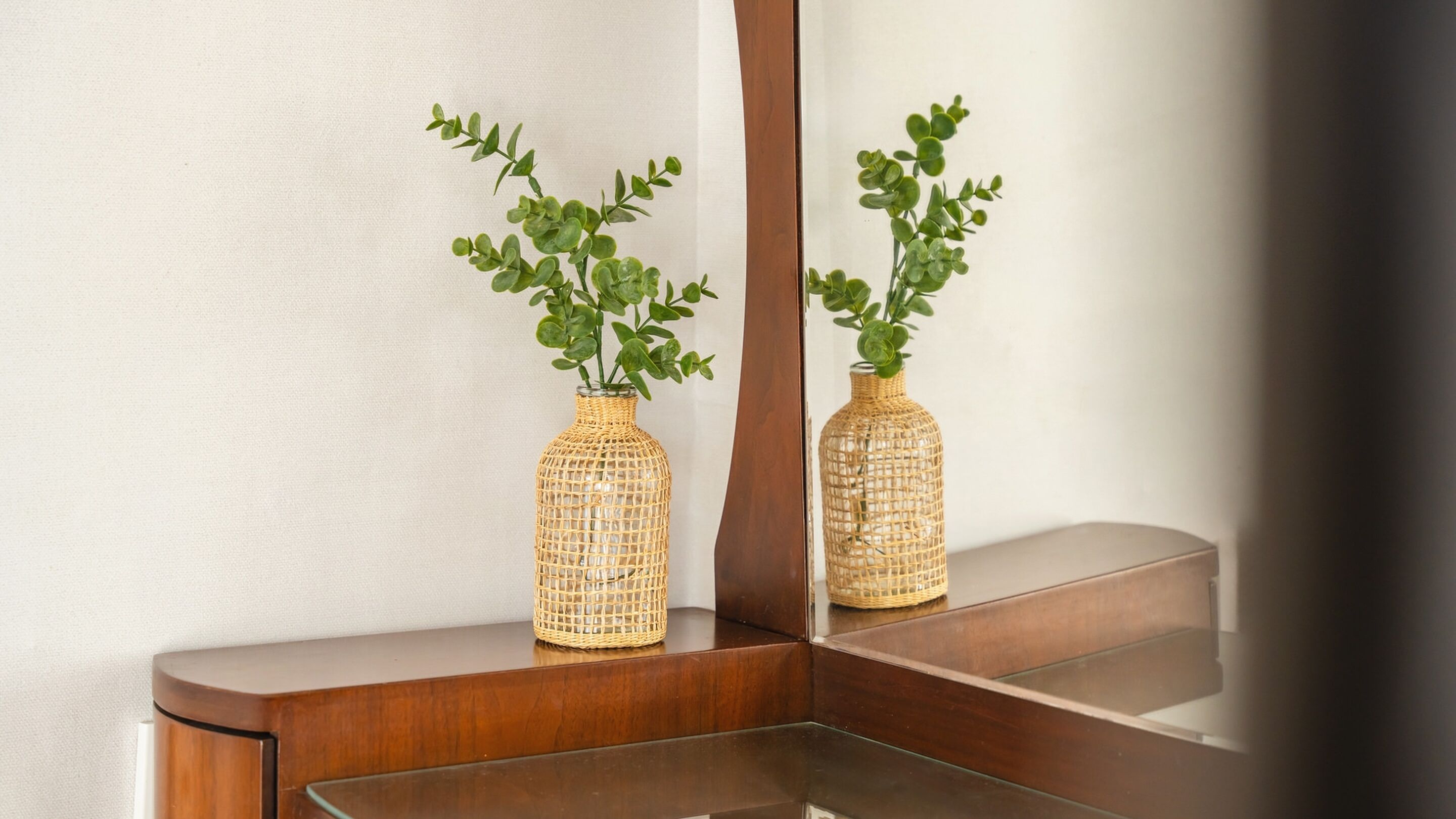 Two woven vases with green plants on a wooden surface, reflecting in a mirror.