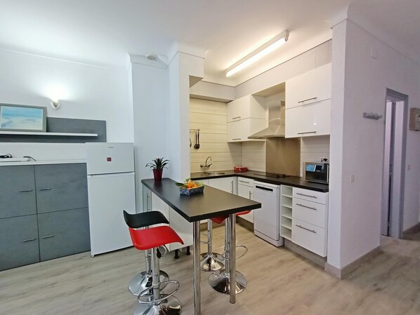 A modern kitchen with white cabinets, a black countertop, and stainless steel appliances. There are two bar stools with red seats and a small potted plant on the counter. - Summer apartment for your holiday in Spain. HUTG-060668 (l'Escala)