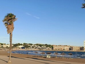Ein Strand mit einer Palme, Strandstühlen und Blick auf eine Küstenstadt.