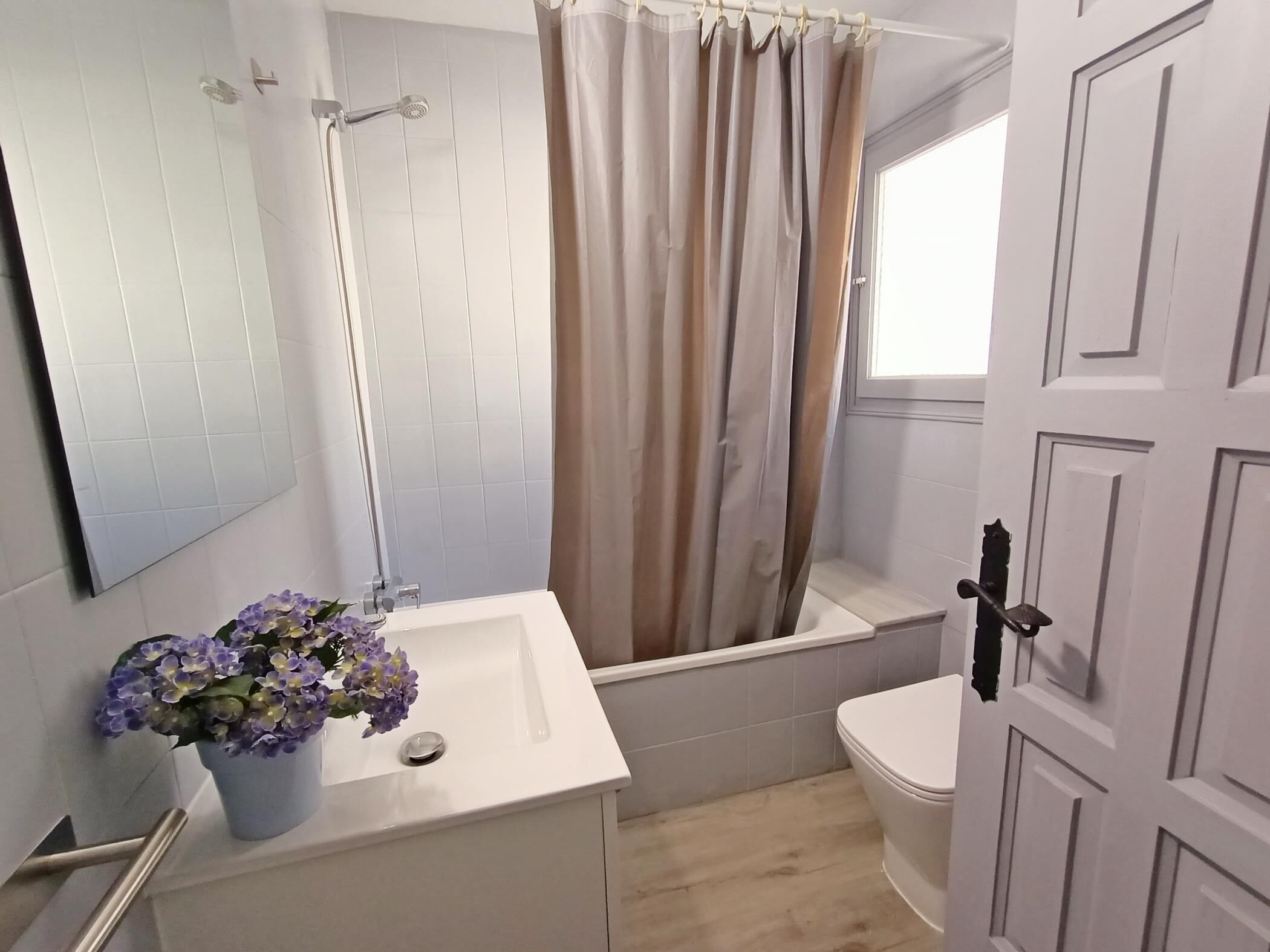 A bathroom with a white sink, a shower, and a toilet. There is a potted plant on the sink and a curtain over the shower.
