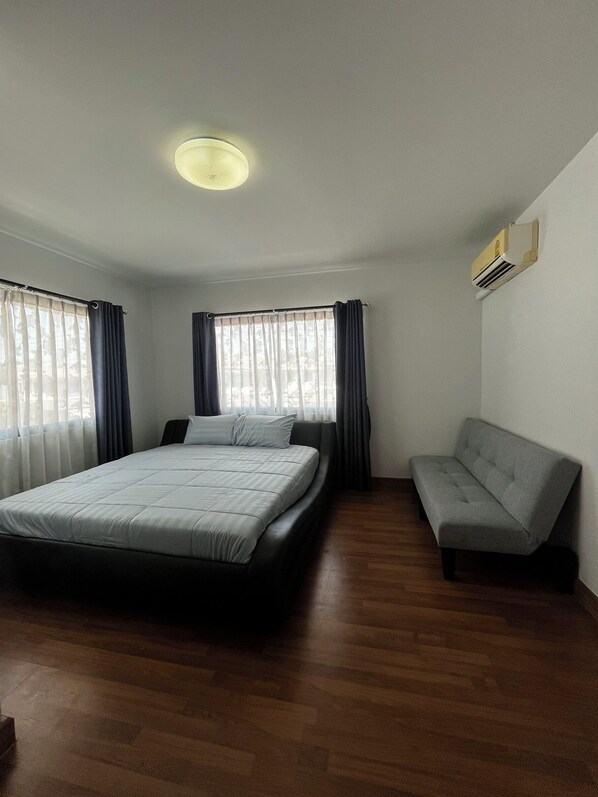 A bedroom with a bed, a sofa, a ceiling light, and an air conditioning unit.