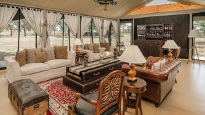 Une pièce aménagée comme un salon, avec un canapé, des fauteuils, une table, un bar et une grande fenêtre.