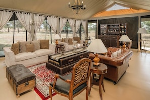 Una habitación con carpa que incluye un sofá, sillones, una mesa, una barra y un amplio ventanal.