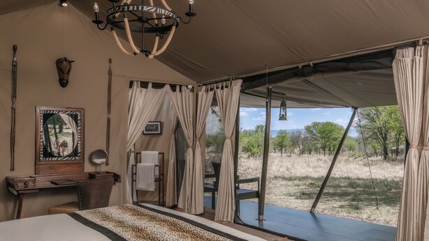 Une pièce aménagée comme une tente, avec un lit, un bureau, une chaise, un lustre, des rideaux et une vue sur l’extérieur.