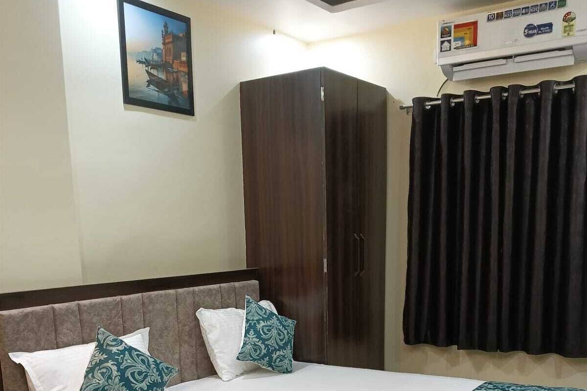 A neatly made bed with a patterned bedspread, a dark wooden wardrobe, and a framed picture on the wall.