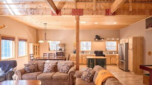 Amplia sala de estar con techo alto, vigas de madera, comedor y cocina equipada con electrodomésticos modernos.