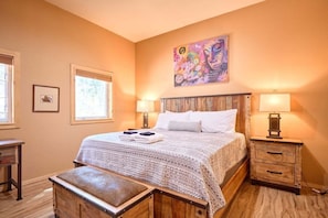 A bedroom with a wooden bed, two bedside tables with lamps, a window, and a painting on the wall.