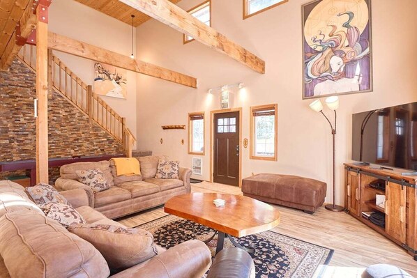 A spacious living area with a wooden staircase, a sofa set, a coffee table, and a television.