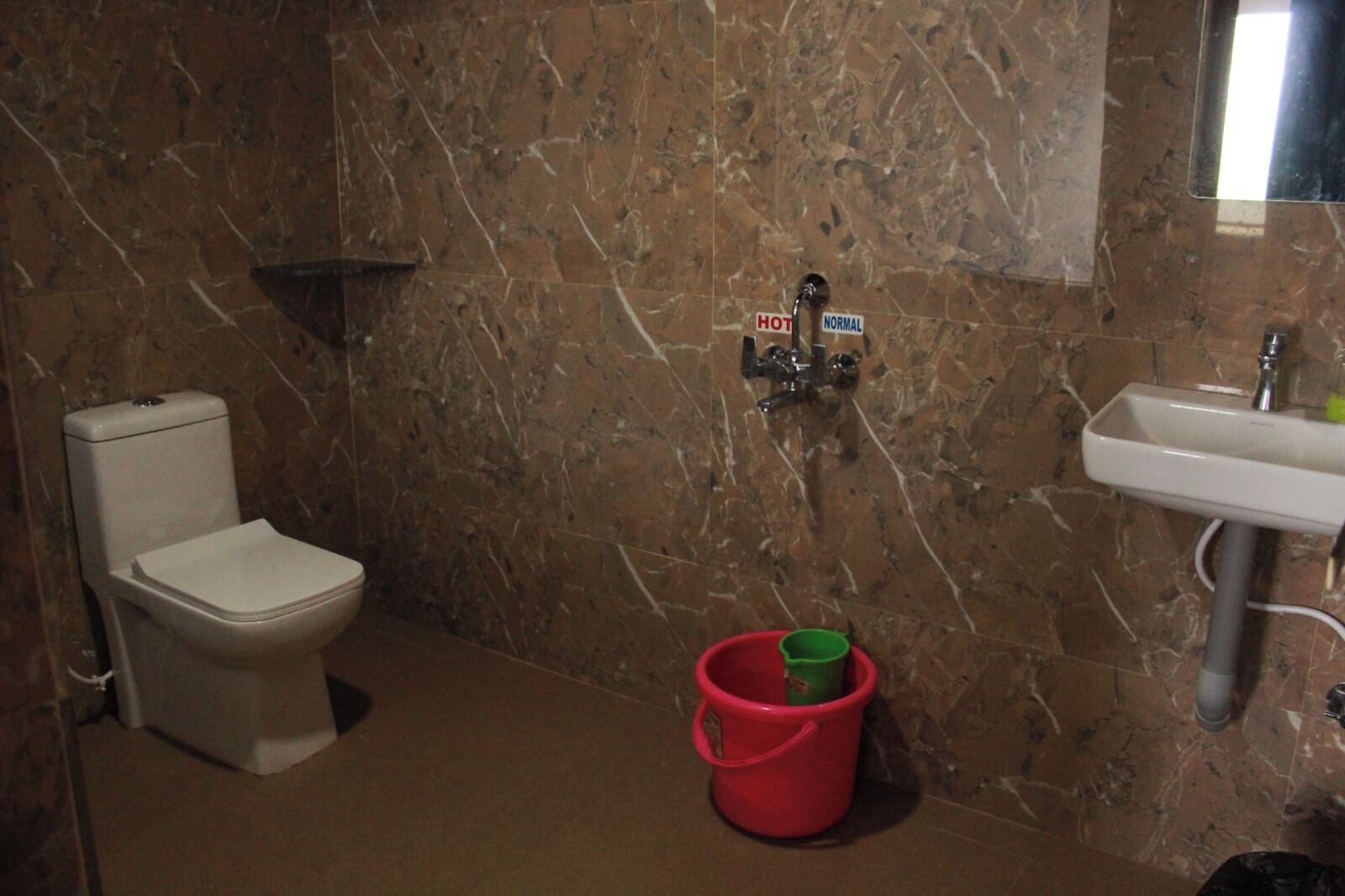 A bathroom with a toilet, a sink, and a shower with a hot and normal water control.