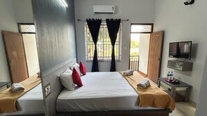 Une chambre d’hôtel avec un grand lit, deux tables de chevet, un ventilateur de plafond, un appareil de climatisation, une télévision et une fenêtre avec des rideaux.