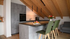 Une cuisine moderne dotée d’un îlot central, d’appareils électroménagers intégrés et de poutres en bois au plafond.