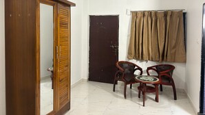 A room with a wooden wardrobe, a dark door, a small round table with two chairs, and a curtain on the wall. - The Blackbuck Ashwem (Ashvem)